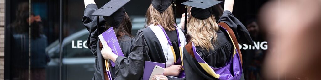 Three students viewed from behind, in caps and gowns during graduation day.
